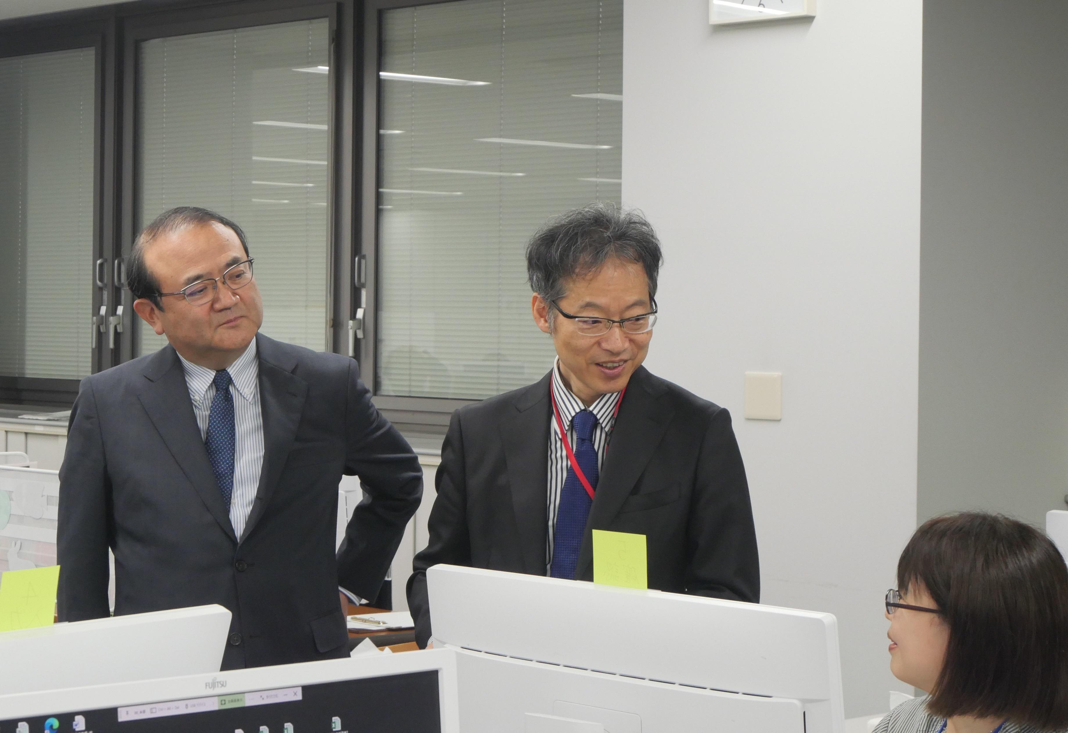写真:職員から説明を受ける藤原文部科学事務次官(中央)と丸山理事長(左)
